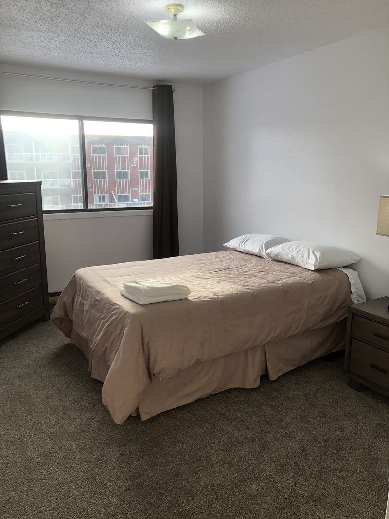 Furnished bedroom with made double bed, dresser, nightstand and window